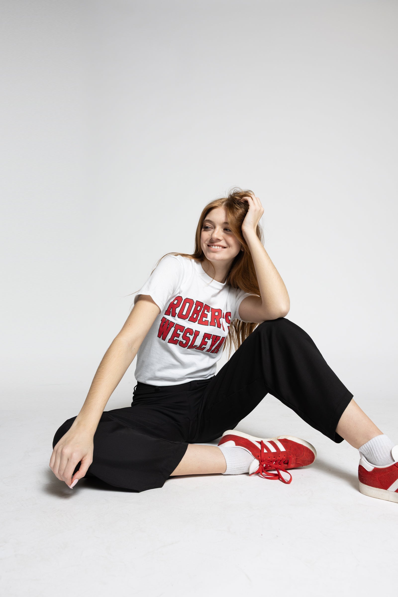 Person wearing a white Roberts Wesleyan t-shirt with red text, black pants, and red sneakers on a white background
