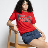 Person wearing a red 'Robert Wesleyan' t-shirt sitting on a wooden chair against a white background