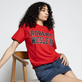 Person wearing a red 'Robert Wesleyan' t-shirt sitting on a wooden chair against a white background