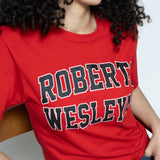 Person wearing a red 'Robert Wesleyan' t-shirt sitting on a wooden chair against a white background