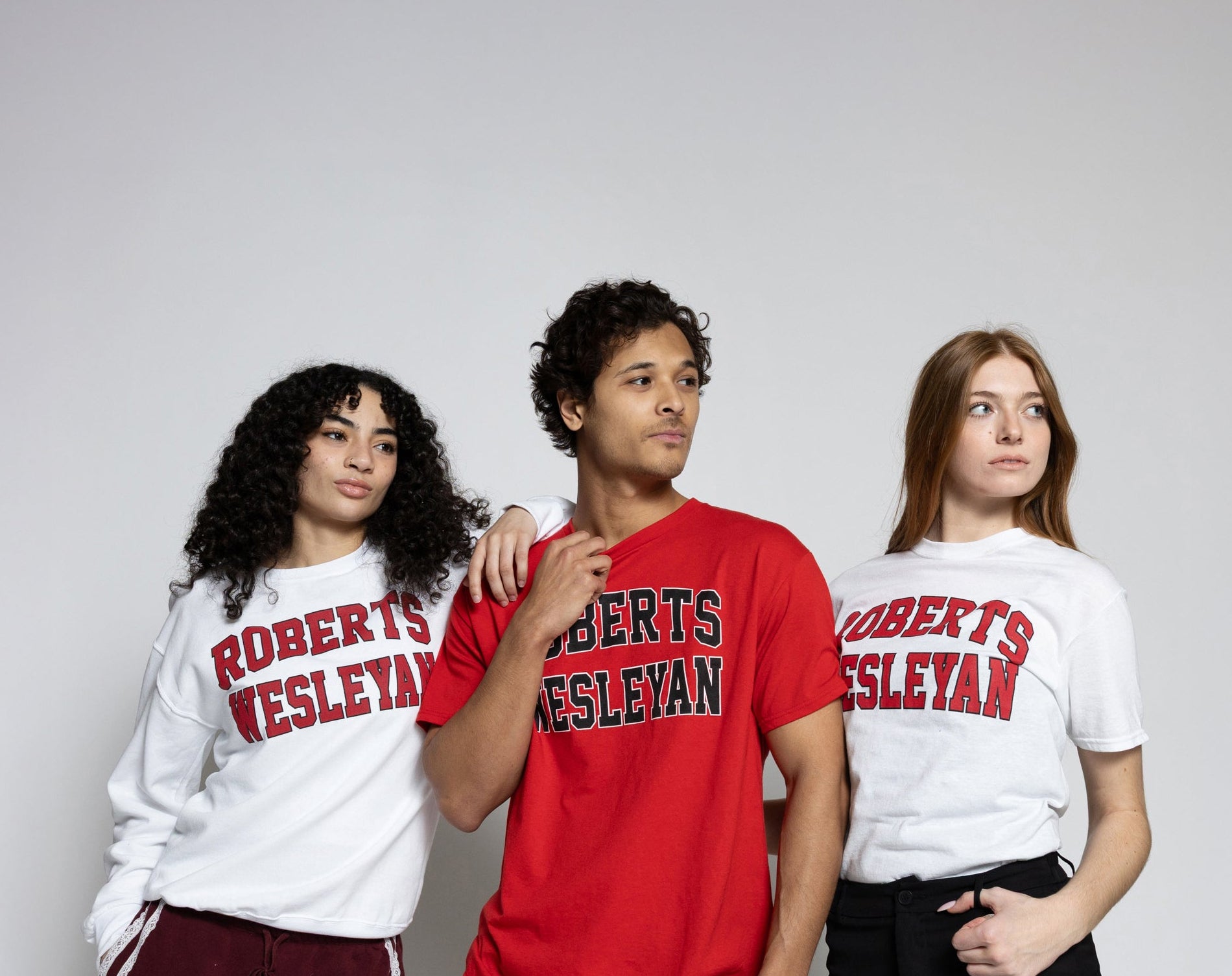 Three people wearing 'Roberts Wesleyan' shirts on a plain background