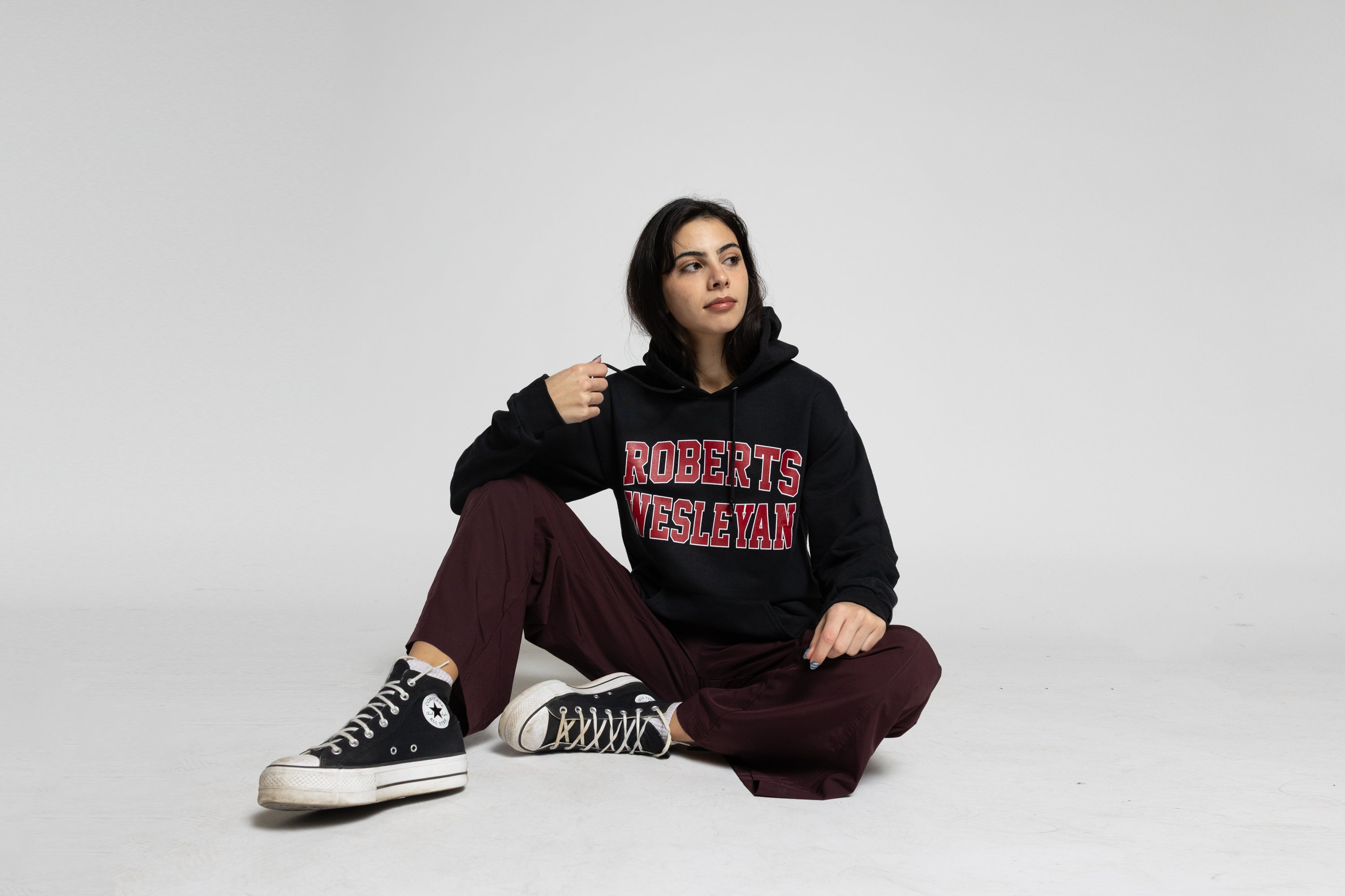 Person wearing a black hoodie with 'Roberts Wesleyan' text, sitting on a white background