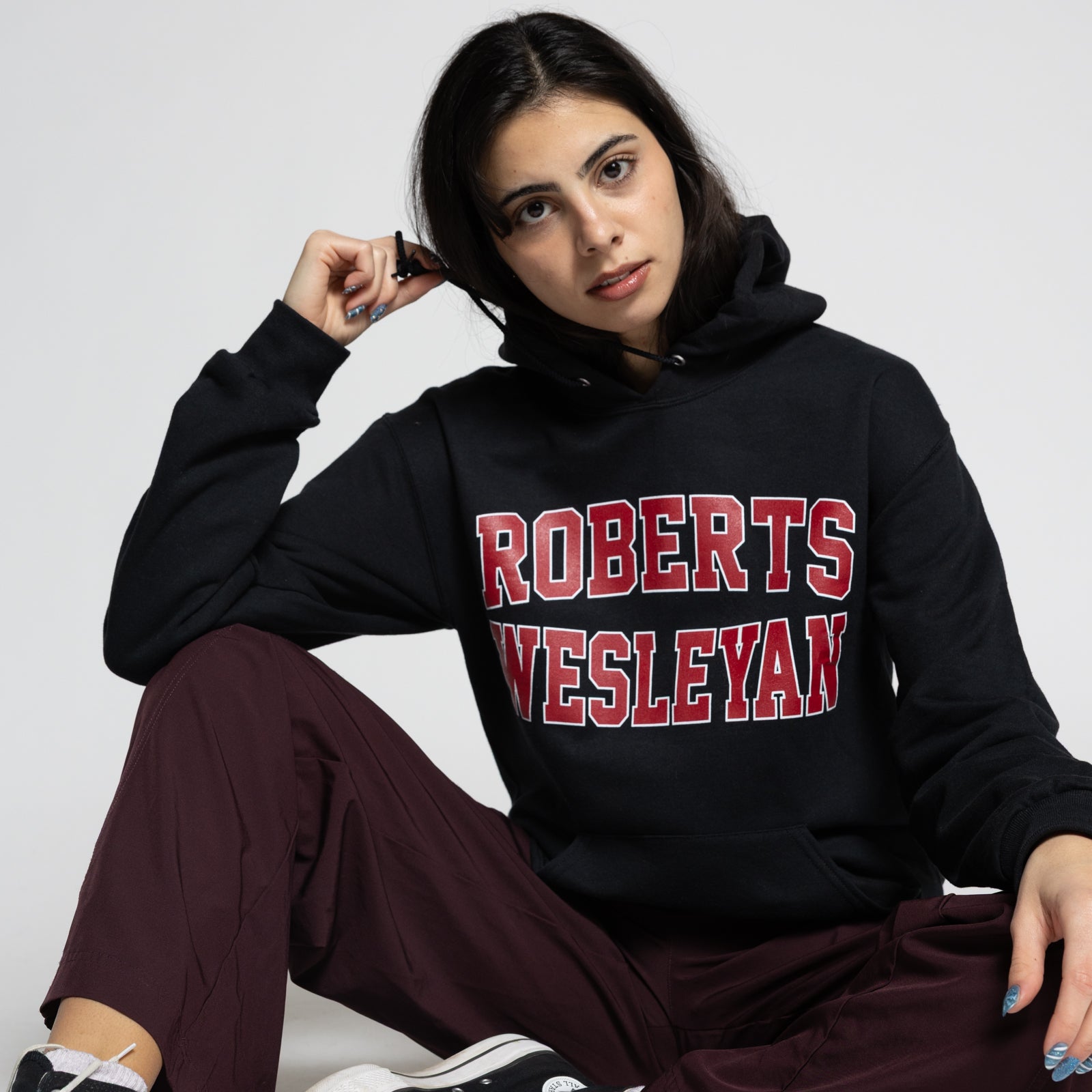 Person wearing a black hoodie with 'Roberts Wesleyan' text, sitting on a white background.