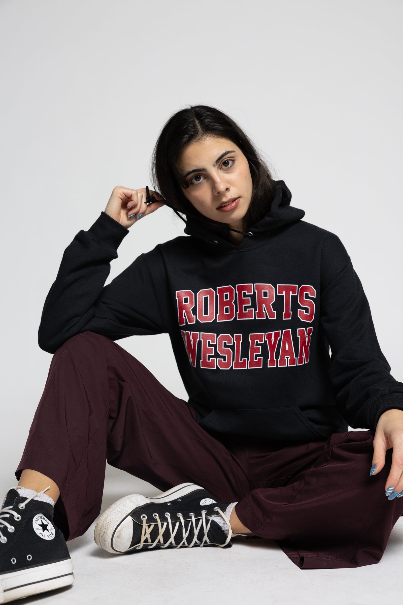 Person wearing a black hoodie with 'Roberts Wesleyan' text, sitting on a white background.